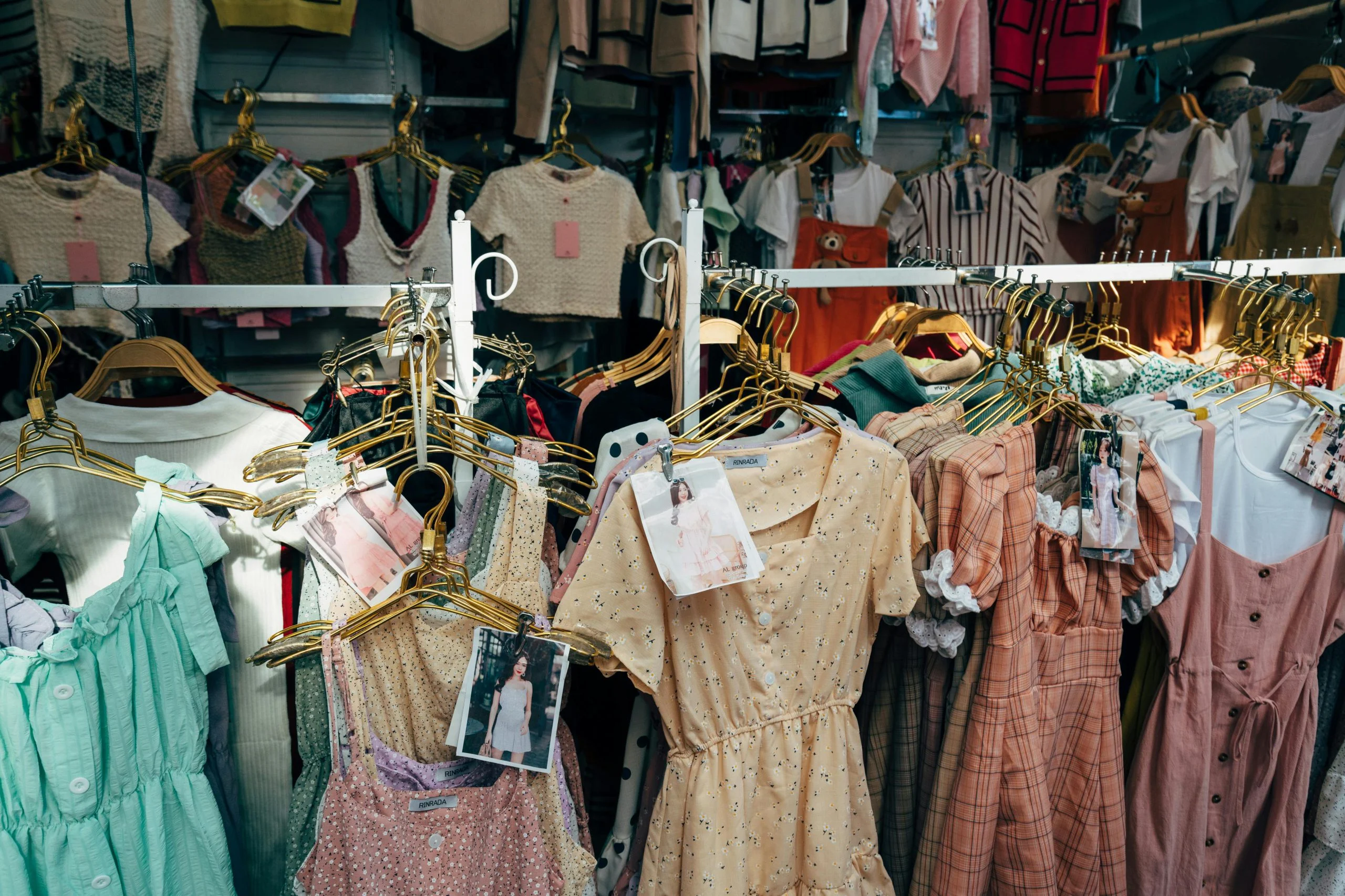 Varios vestidos y blusas de mujer en perchas en una tienda de ropa, mostrando diferentes estilos y colores, incluidos diseños estampados y lisos.